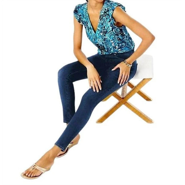 Woman sitting on a chair wearing a blue patterned top and Lilly Pulitzer jeans.