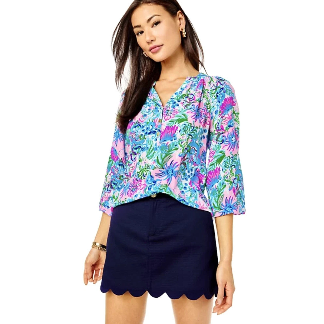 Woman wearing a colorful floral blouse and Lilly Pulitzer navy shorts on a white background