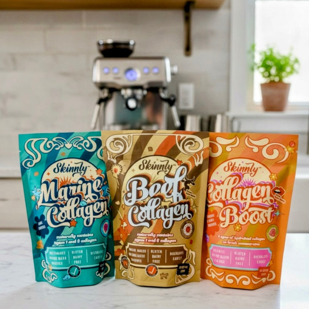 Three packages of Skinny Collagen products on a kitchen counter with an espresso machine in the background.