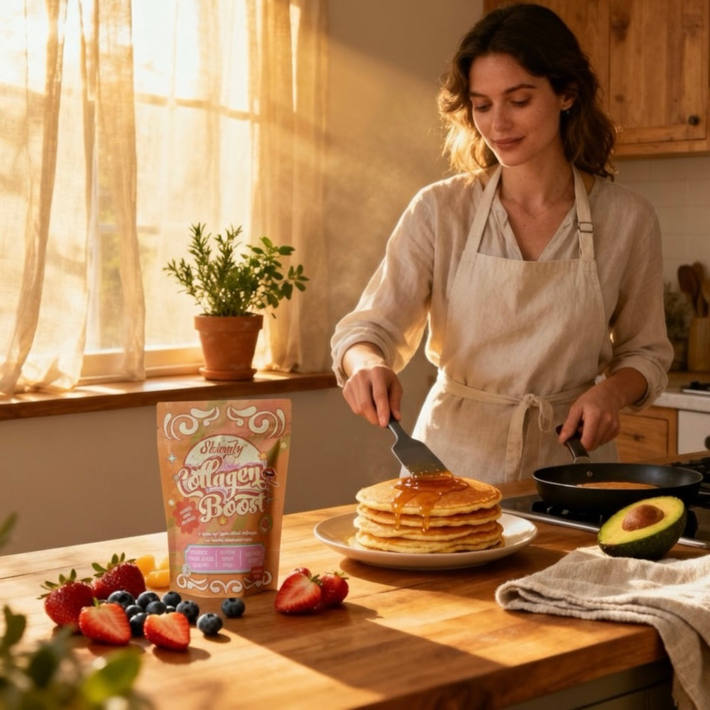 Woman in a kitchen making pancakes with a bag of Skinnly collagen boost on the counter.