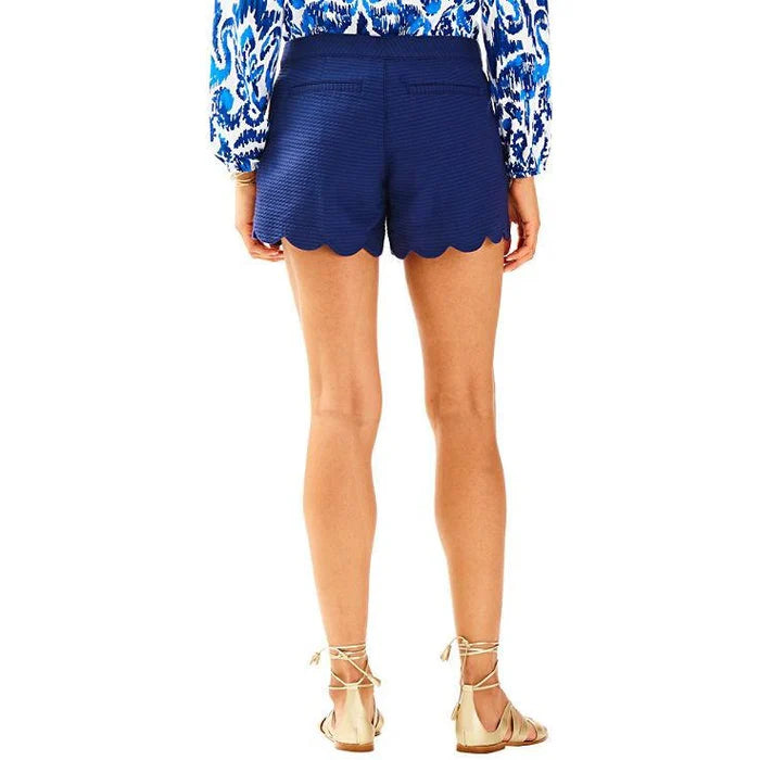 Person wearing Lilly Pulitzer blue scalloped shorts with a white background